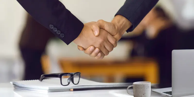 Two business professionals shaking hands over a desk, symbolizing partnership and agreement.
