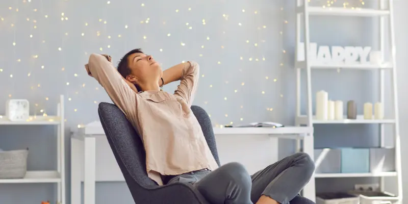 A person sitting back in a chair, arms behind their head, appearing relaxed in a cozy setting